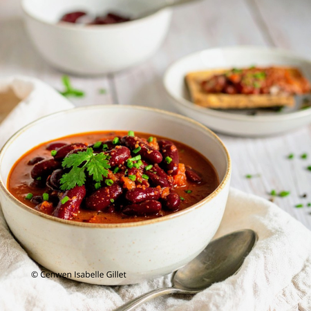 Haricots rouges mijotés dans une sauce tomate épaisse et parfumée, servis dans un bol, herbes fraiches.