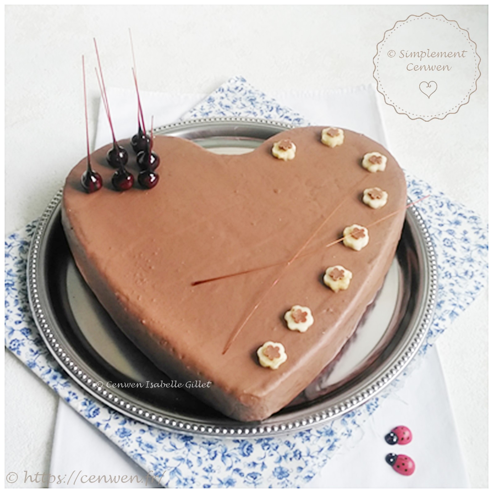 Gâteau en forme de cœur recouvert d’un glaçage chocolat au lait, décoré de fleurs découpées dans des rondelles de banane et de noisettes caramélisées.