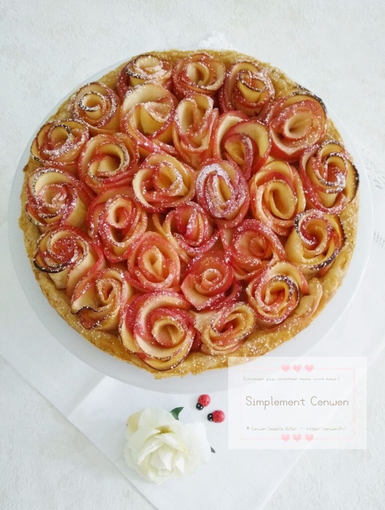 Tarte aux pommes décorée de fines lamelles roulées en roses, légèrement saupoudrée de sucre glace.