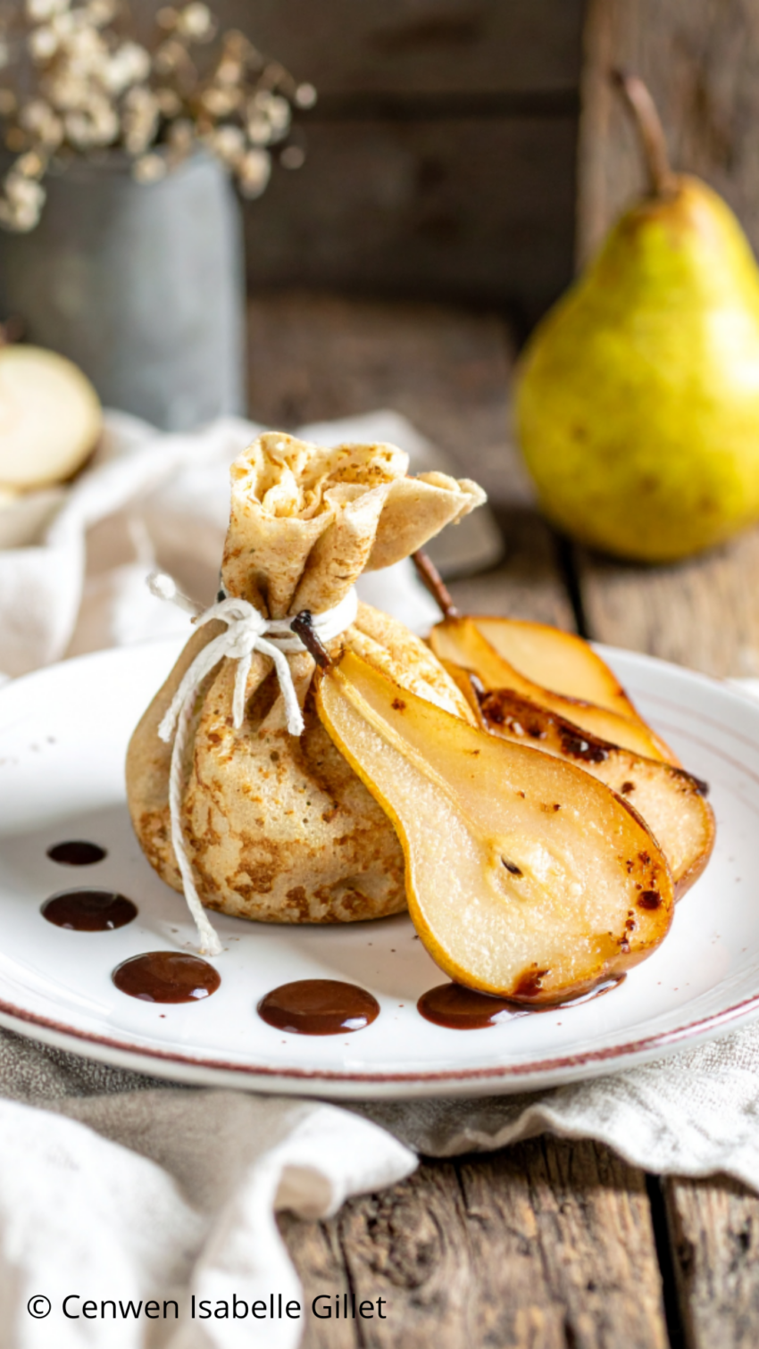 Crêpe nouée en aumônière, poires fraîches et sauce au chocolat sur assiette rustique