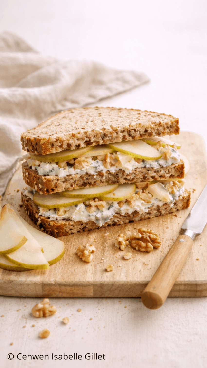 Sandwich au roquefort, poire et noix avec salade, présenté en trois tranches sur une planche.