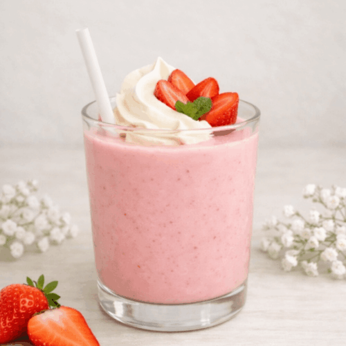 Un verre de milk-shake rose onctueux à la fraise, décoré de crème fouettée, de fraises fraîches et d'une paille blanche.
