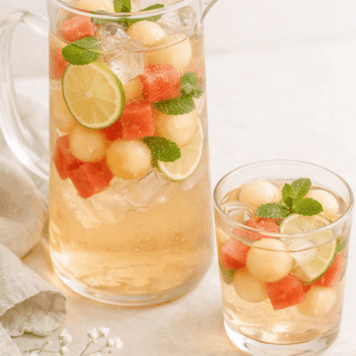 Carafe de thé glacé au melon, pastèque, rondelles de citron vert et feuilles de menthe fraîche avec glaçons.