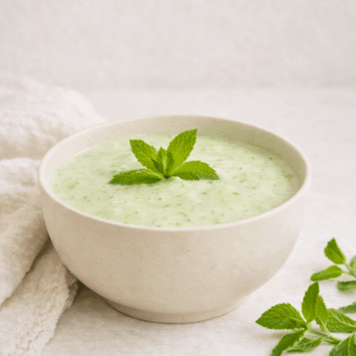 Velouté glacé de concombre et yaourt de soja dans un bol, décoré de feuilles de menthe fraîche